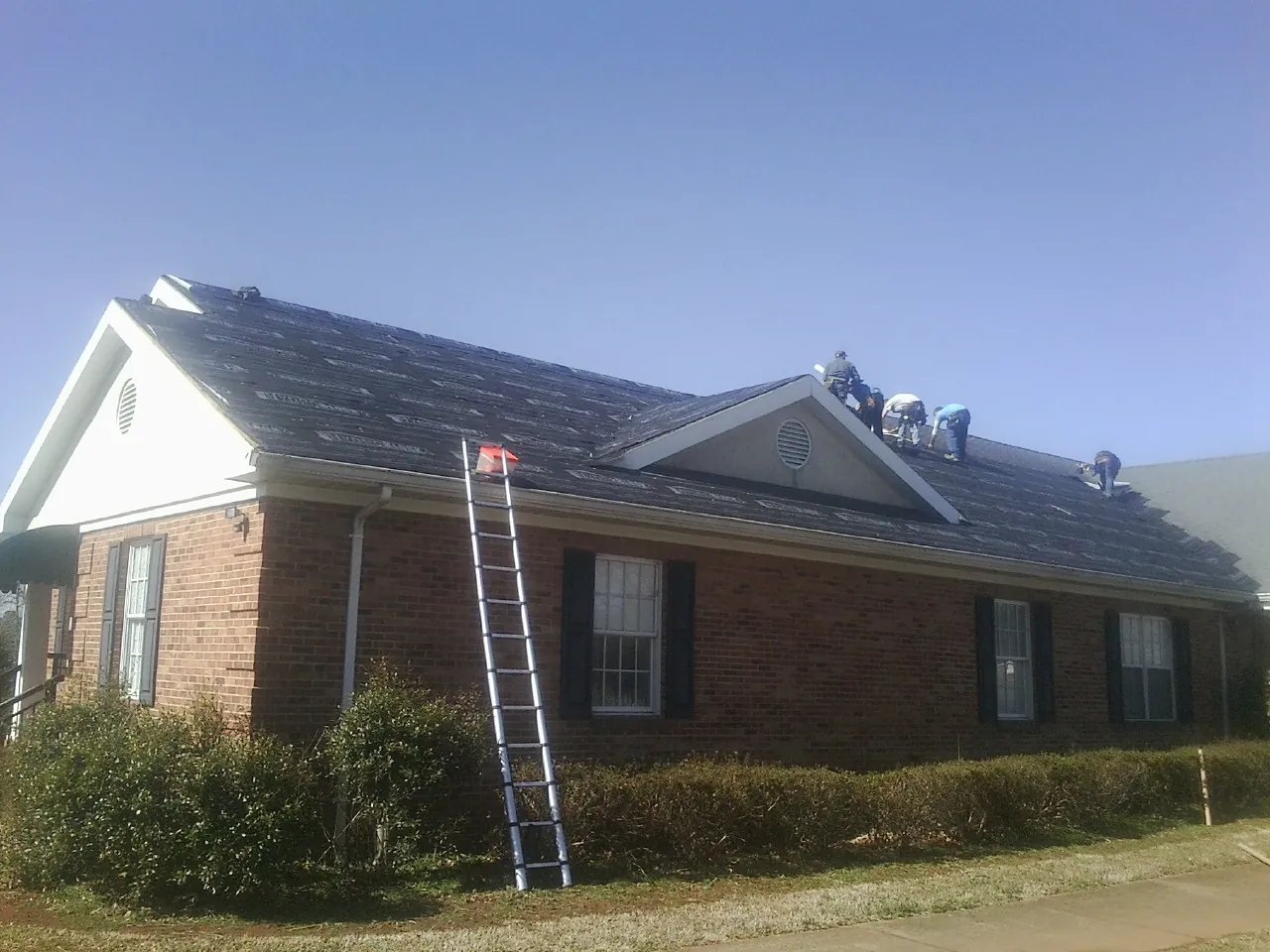 Crew tearing shingles off a brick ranch roof with a ladder set — Metal Roof Repair work by our crew in Stoutsville
