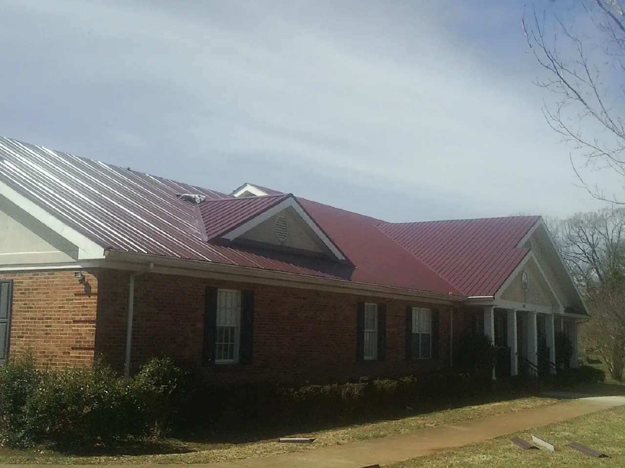 Red metal roof with gabled entries on a long brick building, from a Hail Damage Roof Repair job in Stoutsville