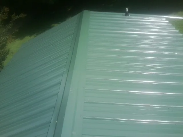 New green metal panels meeting at the ridge of a roof — Flat Roof Repair work by our crew in Stoutsville