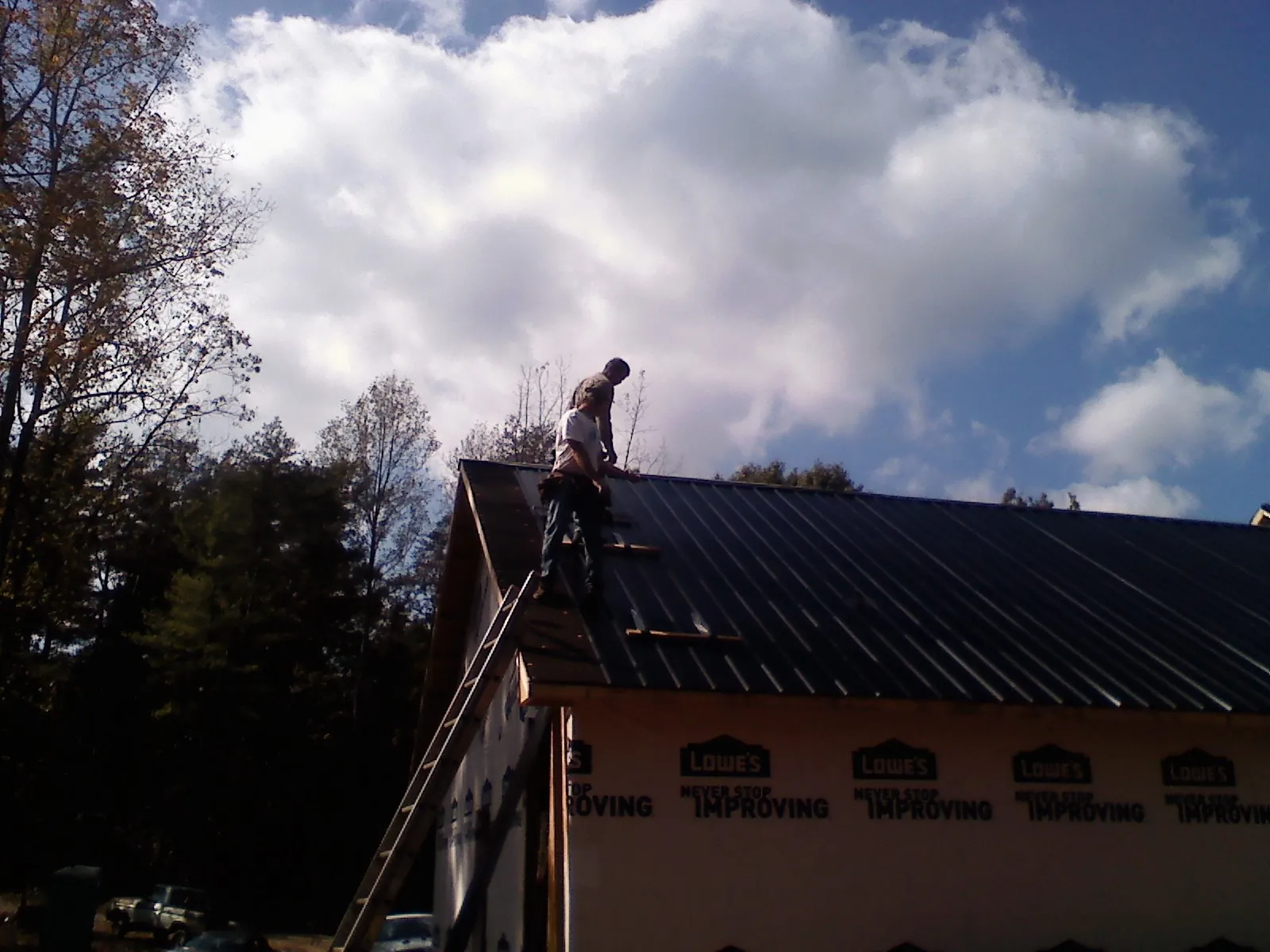 Roofer fastening dark metal panels high against a cloudy sky, from a Roof Inspection job in Stoutsville
