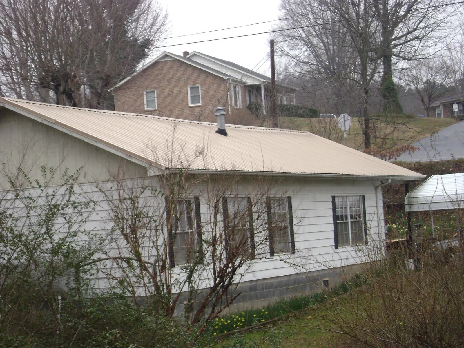 Tan metal roof on a white sided house set into a hillside — Commercial Roofing by Roofing Brothers in Stoutsville